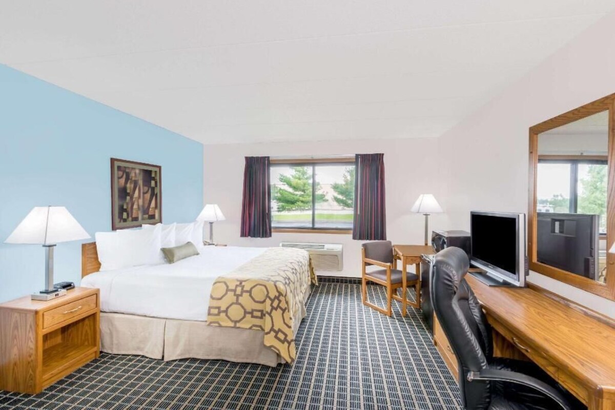Una habitación de hotel con cama, escritorio, silla, televisor y ventana con cortinas.