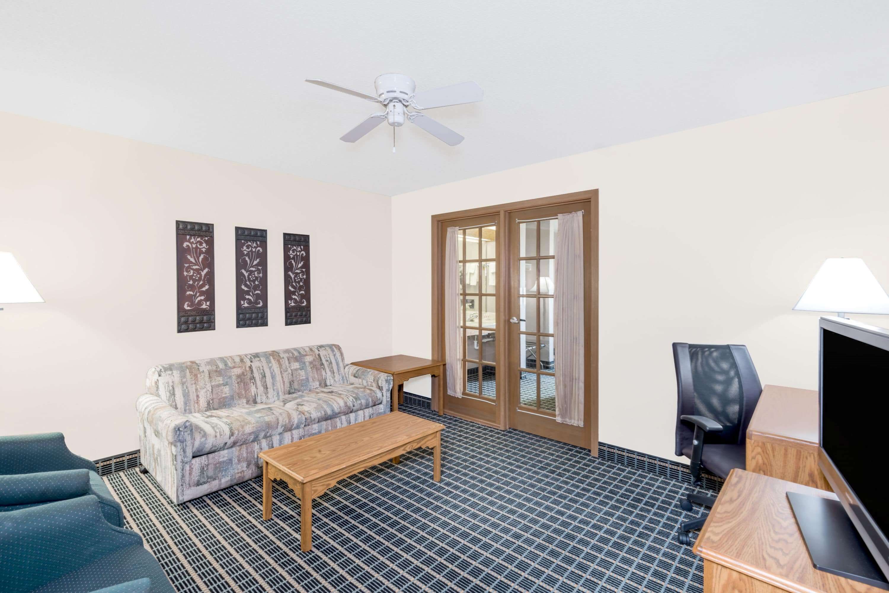 A room with a sofa, a coffee table, a TV, and a ceiling fan.