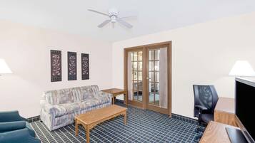 A room with a sofa, a coffee table, a TV, and a ceiling fan.