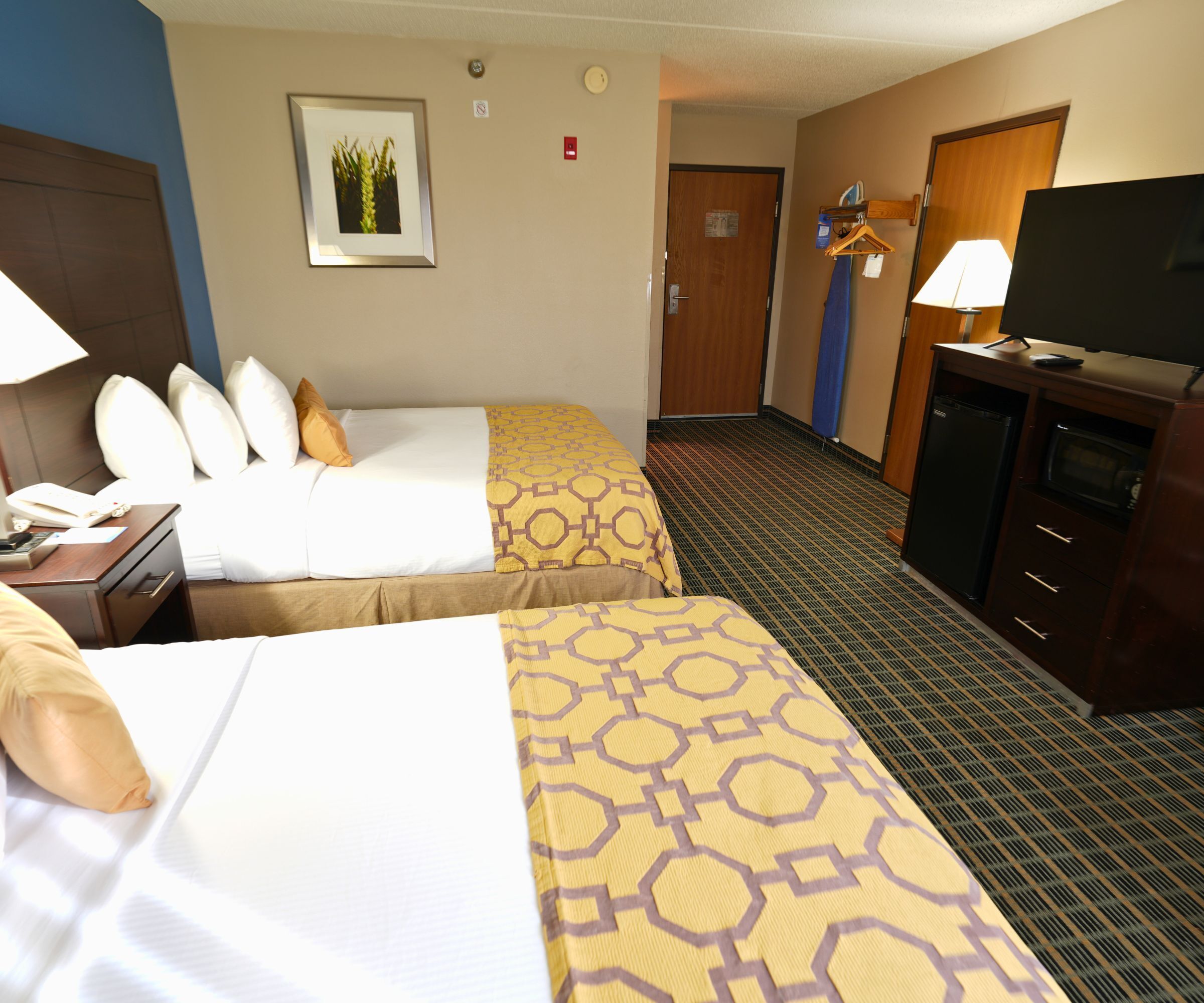 A hotel room with two beds, a desk with a lamp, a television, and a dresser.