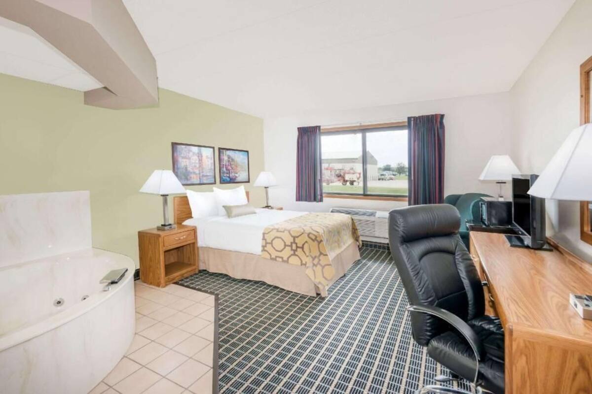 Habitación de hotel con cama, escritorio, silla, televisión y ventana con cortinas.