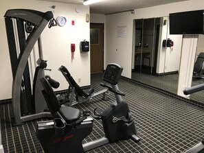 Un gimnasio con equipo cardiovascular, un reloj de pared y un cartel con las normas de seguridad.