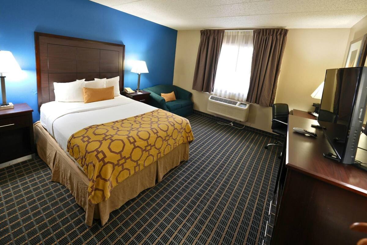 Habitación de hotel con una cama grande, un escritorio, una silla, un televisor y una ventana con cortinas.