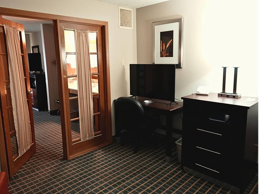 Ein Hotelzimmer mit Schreibtisch, Stuhl, Kommode, einem gerahmten Bild an der Wand und einem gemusterten Teppich.