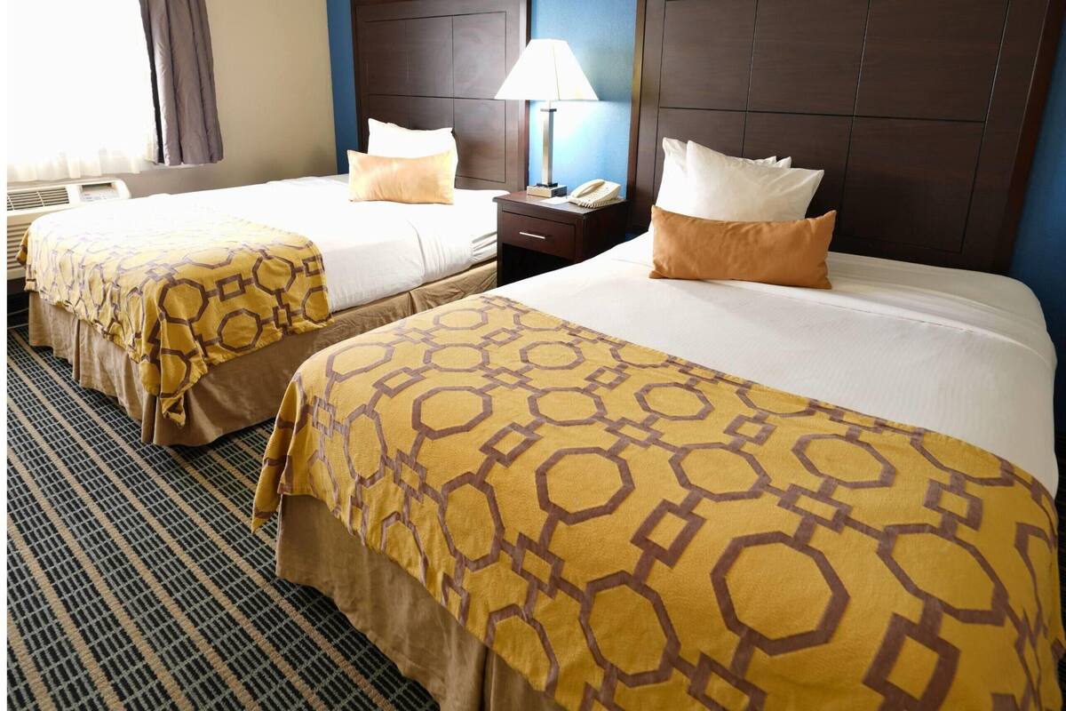Una habitación de hotel con dos camas, una mesita de noche con lámpara y un ventanal con cortinas.