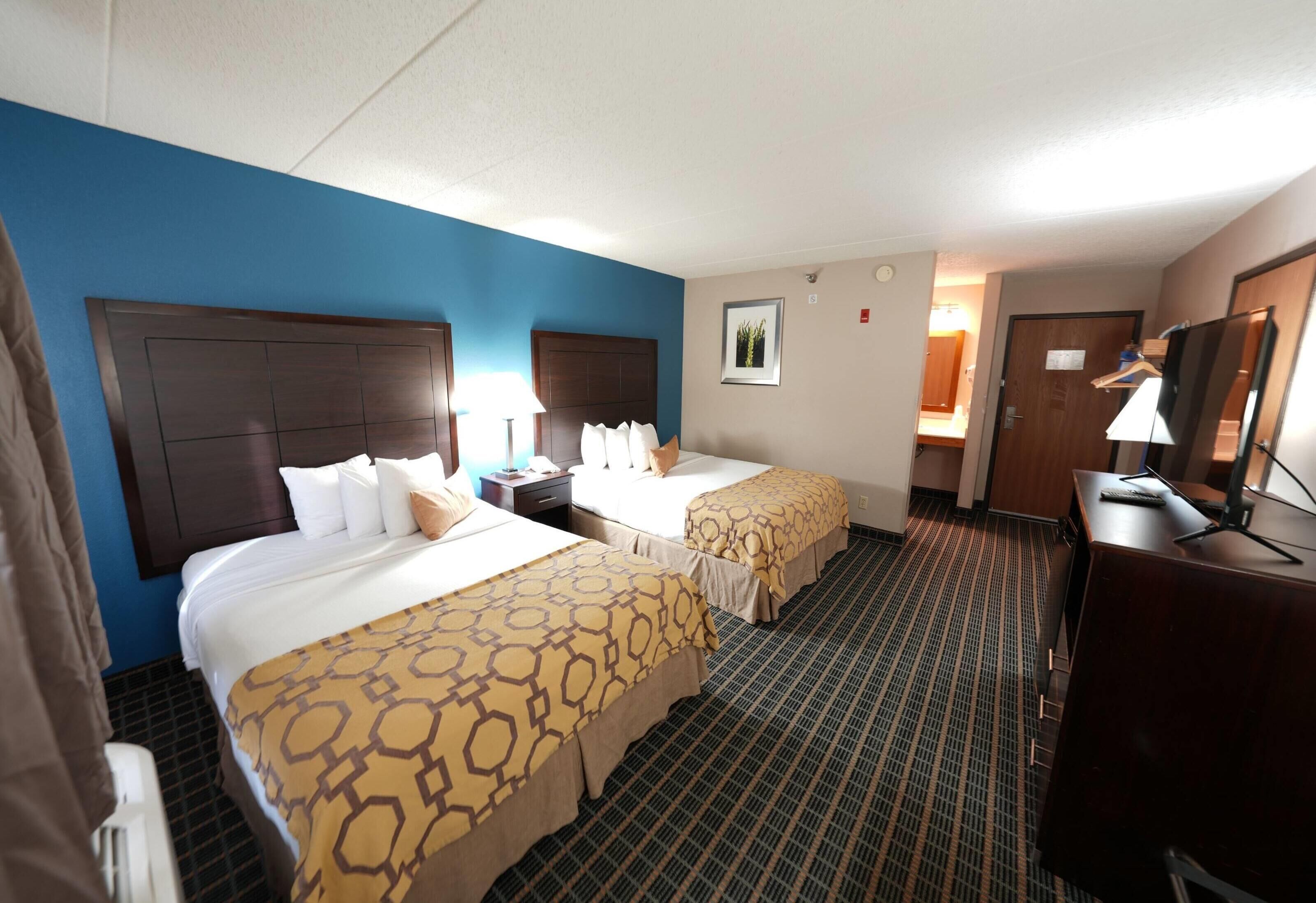 A hotel room with two beds, a desk, a chair, a TV, and a bathroom door.