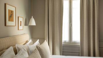 Quarto de hotel com cama, almofadas, luminária pendente e cortinas.