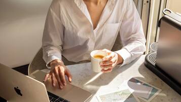 A person using a laptop at a table with a cup of coffee, papers, and a speaker.