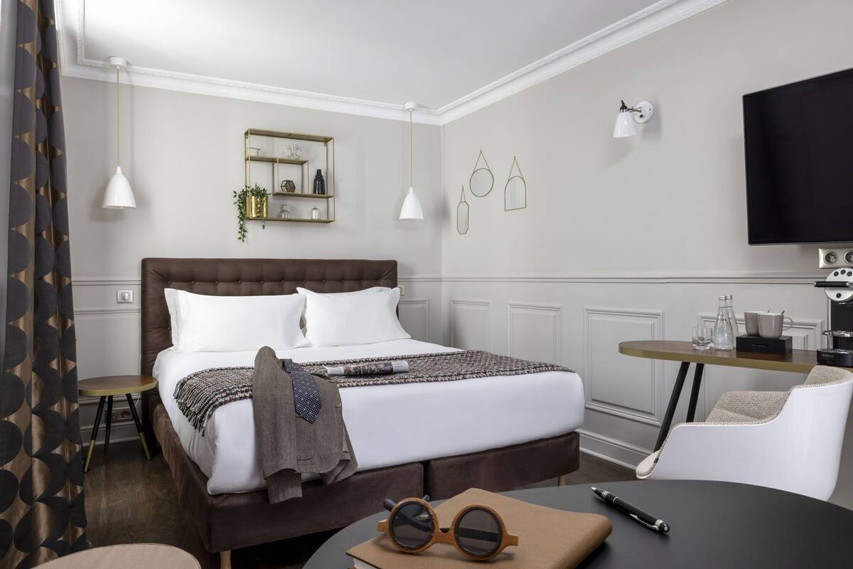 Una habitación de hotel con una cama grande, un escritorio con una silla, un televisor y una cafetera.