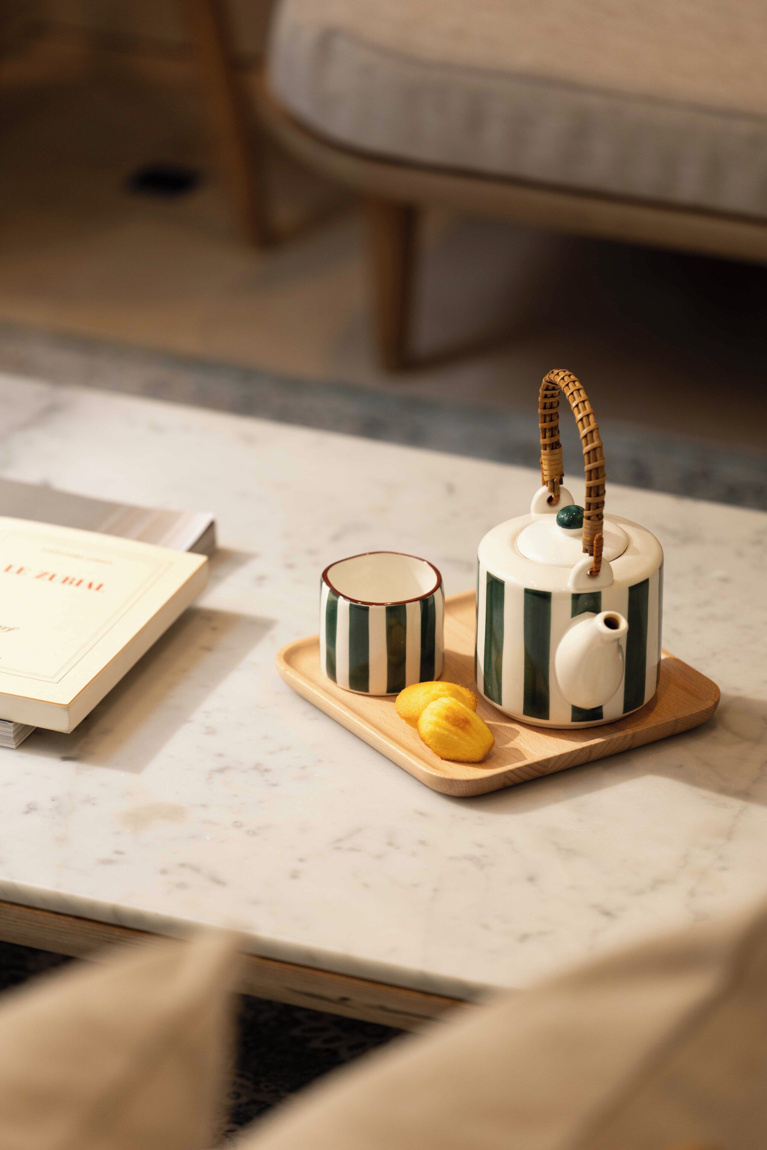 A kitchen area with a marble countertop, a book, a striped teapot, a cup, and a tray with two pastries.