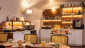 A modern kitchen with wooden cabinets, a dining area with wicker chairs, and a variety of kitchen appliances and utensils. - Hôtel Madeleine Haussmann (Paris)