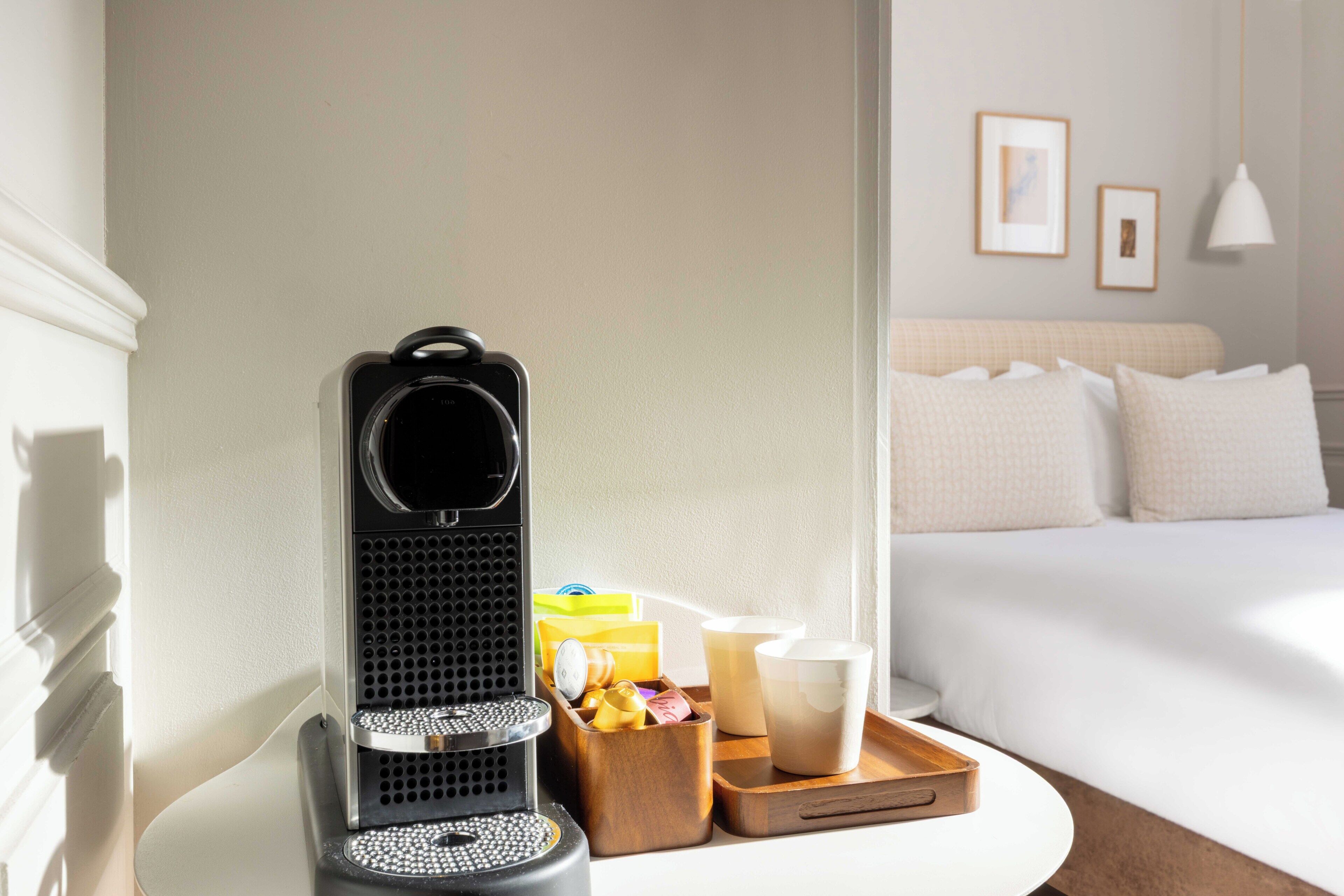 A coffee maker, a tray with cups and a box of tissues, and a bed in a hotel room.