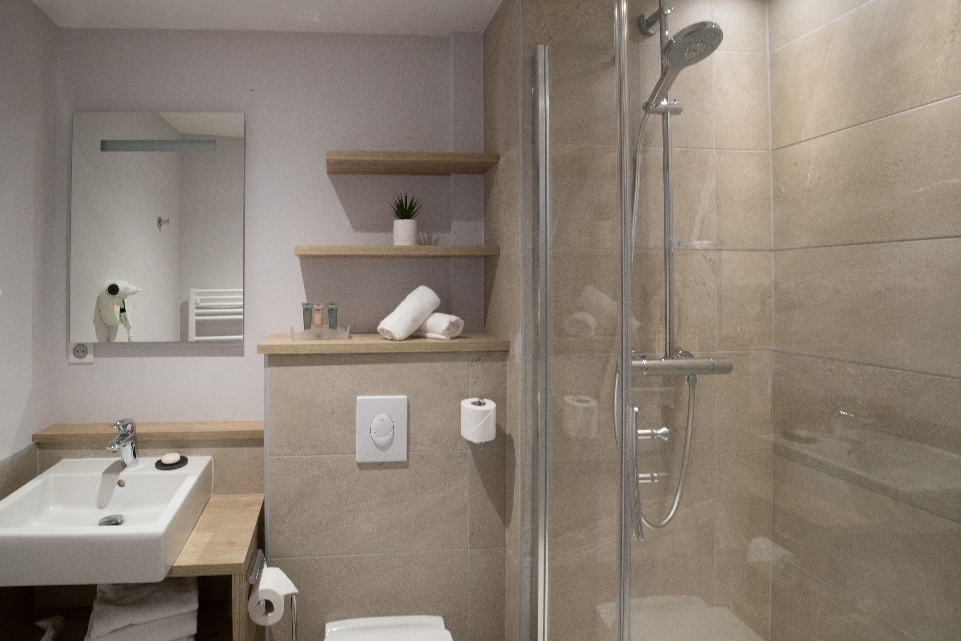 A modern bathroom with a sink, mirror, towel rack, shower, and toilet.