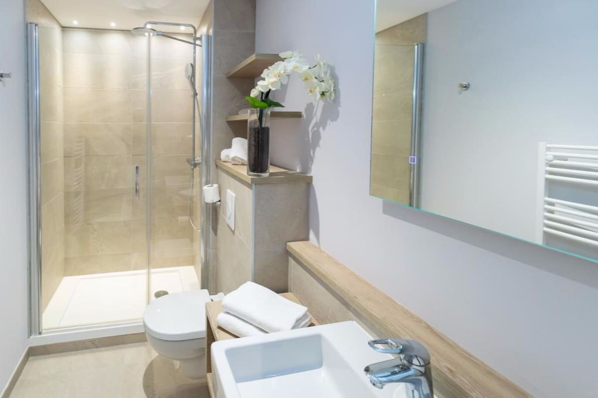 Et moderne badeværelse med en glasafskærmet brusekabine, et hvidt toilet, en vask og et spejl.
