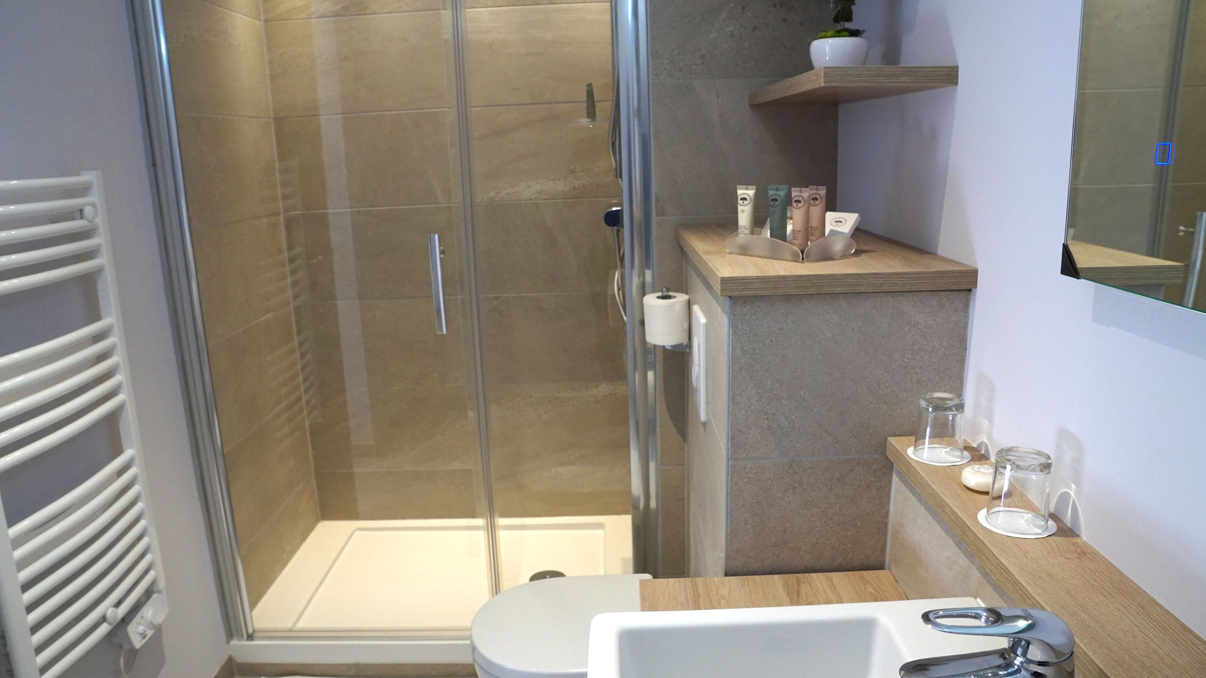 Un baño moderno con ducha envuelta en vidrio, un lavamanos blanco y un estante con artículos de aseo.