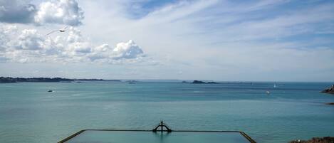 Una playa con cielo despejado, mar tranquilo y una estructura de muelle.