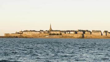 A coastal cityscape with a prominent castle-like structure, a body of water in the foreground, and a clear sky.