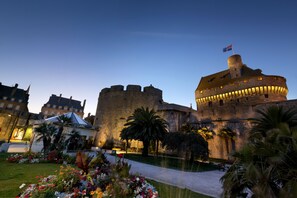 Un castillo histórico con una torre redonda, rodeado de jardines cuidados y un paseo empedrado.
