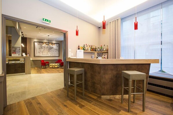 Zona de bar moderna con una barra de madera, dos taburetes y una estantería llena de botellas.