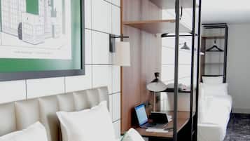 Une chambre d’hôtel avec un lit, un bureau, un ordinateur portable et une reproduction encadrée d’un plan architectural accrochée au mur.