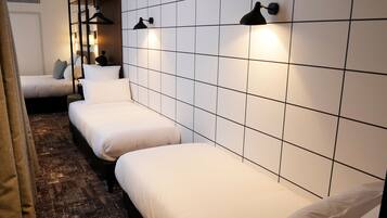 A hotel room with three single beds aligned against a tiled wall, each with a black wall-mounted lamp.