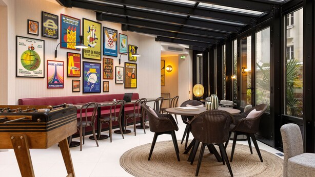 A dining area with a round table, chairs, a foosball table, and a red bench. - Hotel Moderniste (Paris)
