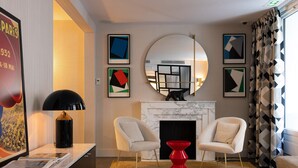 A modern living room with a fireplace, two armchairs, a red and green side table, and abstract artwork on the walls. - Hotel Moderniste (Paris)