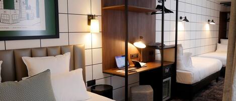A hotel room with a bed, a desk with a laptop, a mirror, and two bedside tables.