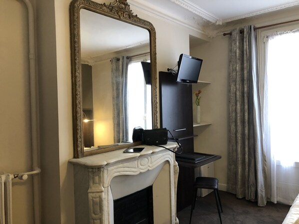 A room with a large ornate mirror, a fireplace, a television on a stand, and a desk with a chair. - Hotel Corona Rodier Paris (Paris)