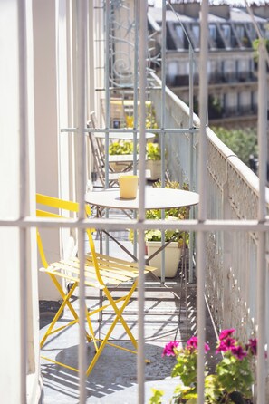 Ein Balkon mit gelben Stühlen und einem Tisch, umgeben von Metallgeländern und Blumentöpfen.