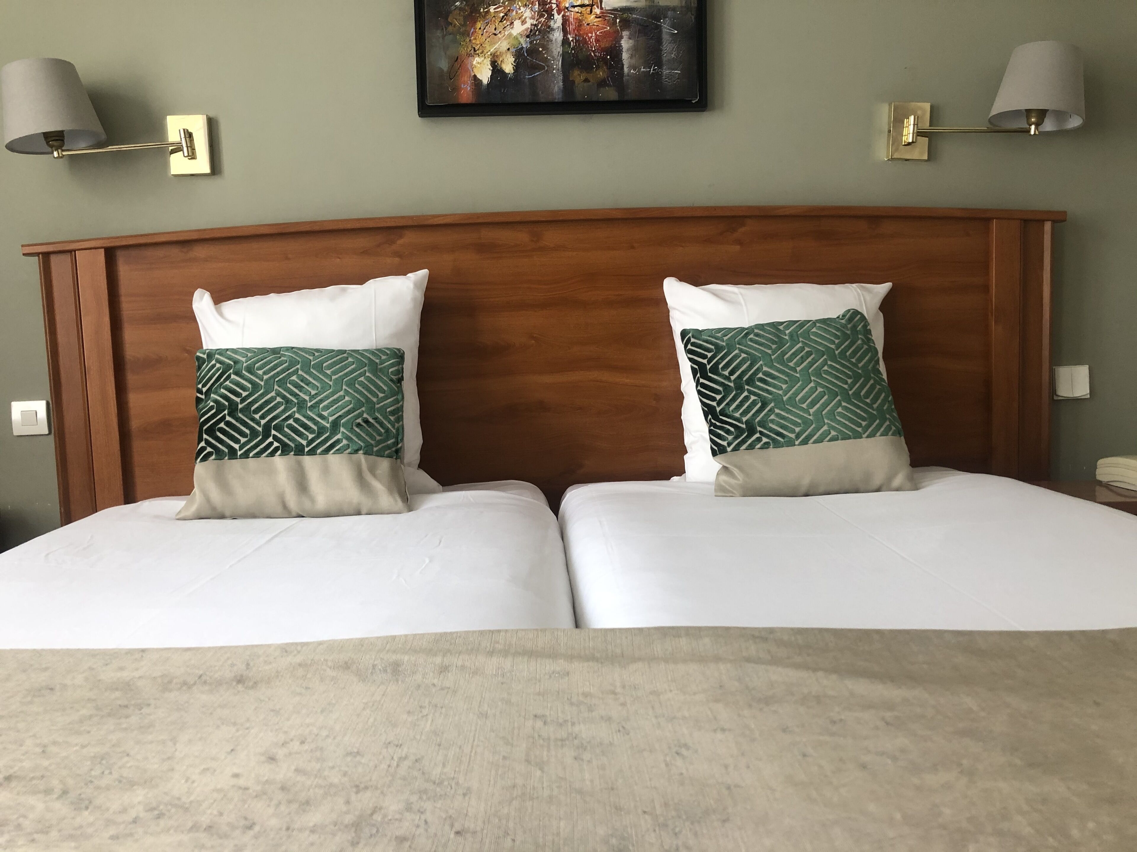 Cama doble con dos almohadas, cabecera de madera y dos lámparas fijadas a la pared.