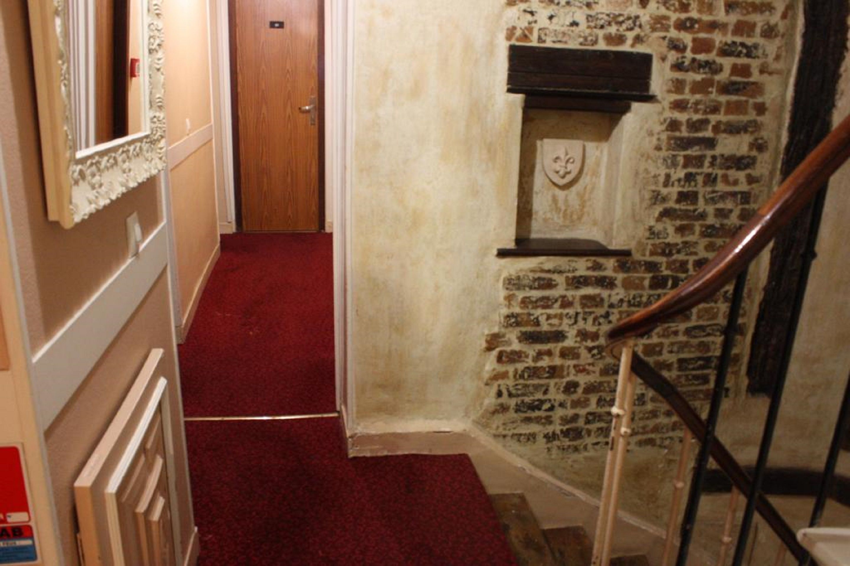 A narrow hallway with a red carpet, a wooden door, and a brick wall with a fireplace.