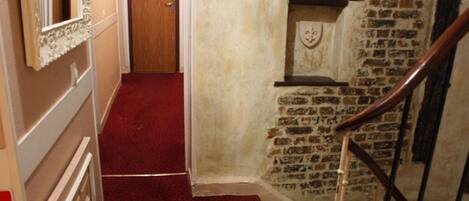 A narrow hallway with a red carpet, a wooden door, and a brick wall with a fireplace.