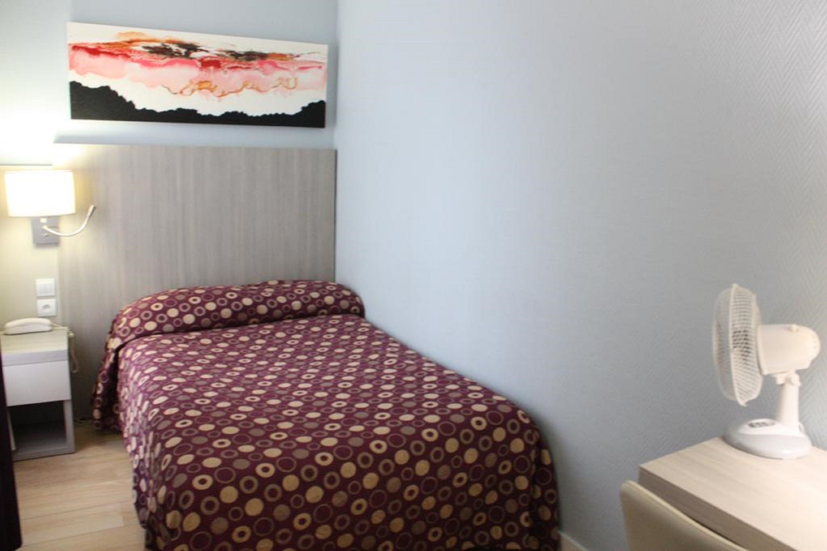 Une chambre d’hôtel avec un lit, une table de chevet, une lampe et un tableau accroché au mur.