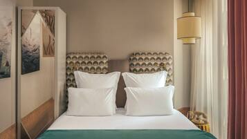 A hotel room with a large bed, two pillows, a green bedspread, a headboard with a patterned design, a wall-mounted artwork, a bedside lamp, and a vintage telephone on a side table.