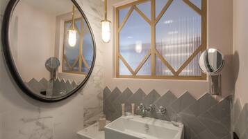 A bathroom with a large round mirror, a rectangular mirror, a bathtub, and a window with a geometric frame.
