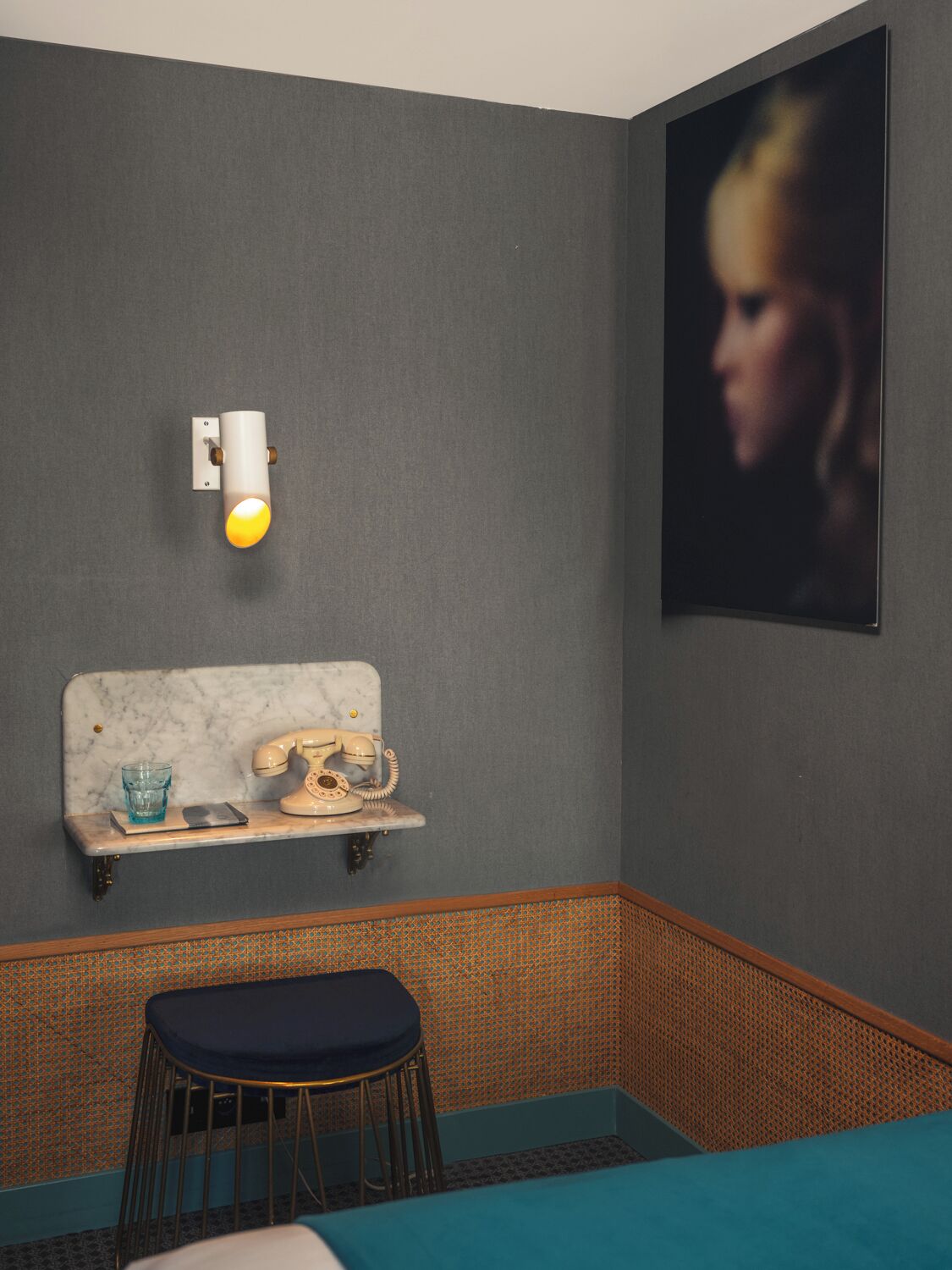 A room with a marble headboard, a vintage telephone, a small shelf with a glass, and a stool.