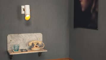 A room with a marble headboard, a vintage telephone, a small shelf with a glass, and a stool.