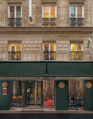 A building with a green awning, multiple windows with ornate black railings, and a visible entrance with a glass door. - Handsome Hotel  (Paris)