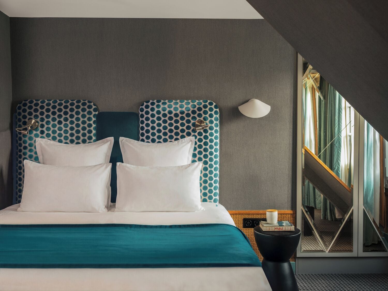 Una habitación de hotel moderna con una cama grande, ropa de cama color turquesa y un cabecero con estampado geométrico.