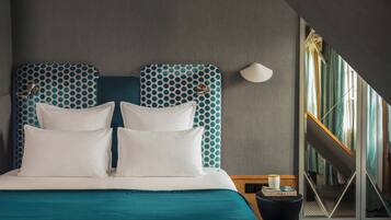 Una habitación de hotel moderna con una cama grande, ropa de cama color turquesa y un cabecero con estampado geométrico.