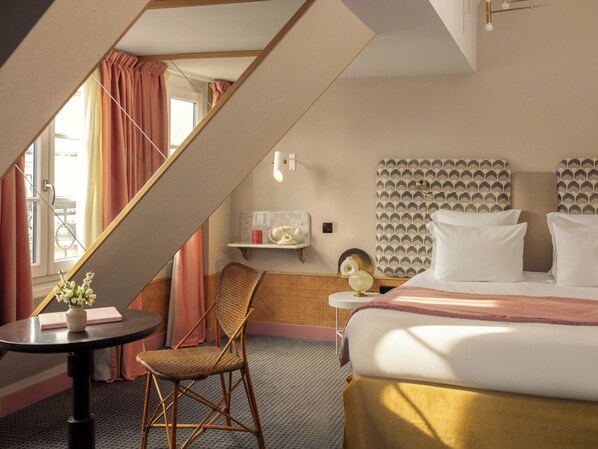 A hotel room with a bed, a chair, a small table, and a window with curtains. - Handsome Hotel  (Paris)