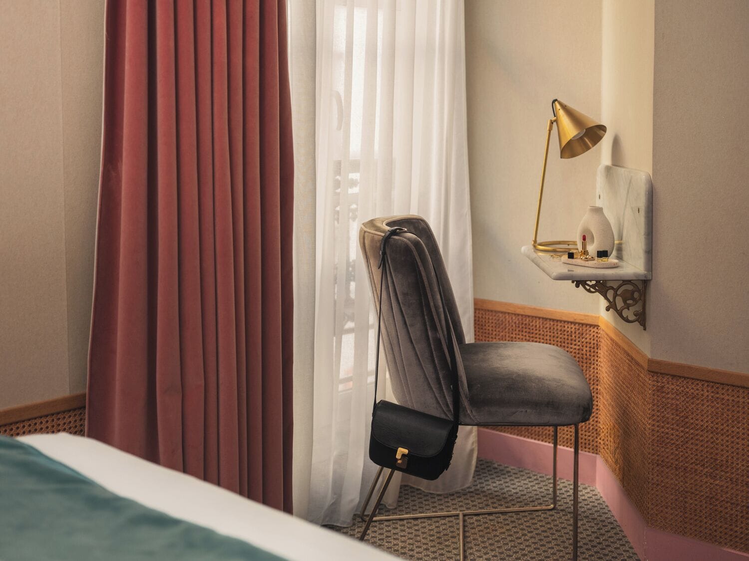 A hotel room with a bed, a chair, a desk with a lamp, and a window with curtains.