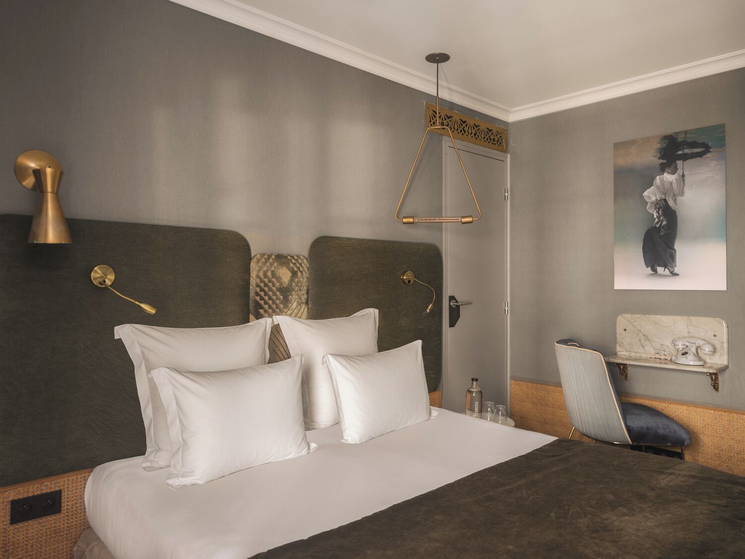 Une chambre d’hôtel avec un grand lit, une chaise, une petite table avec un téléphone et un tableau au mur.
