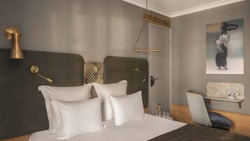 A hotel room with a large bed, a chair, a small table with a telephone, and a painting on the wall.