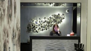Una moderna zona de recepción con piso a cuadros blanco y negro, una pared reflectante con diseño floral y un mostrador con juego de cuchillos.