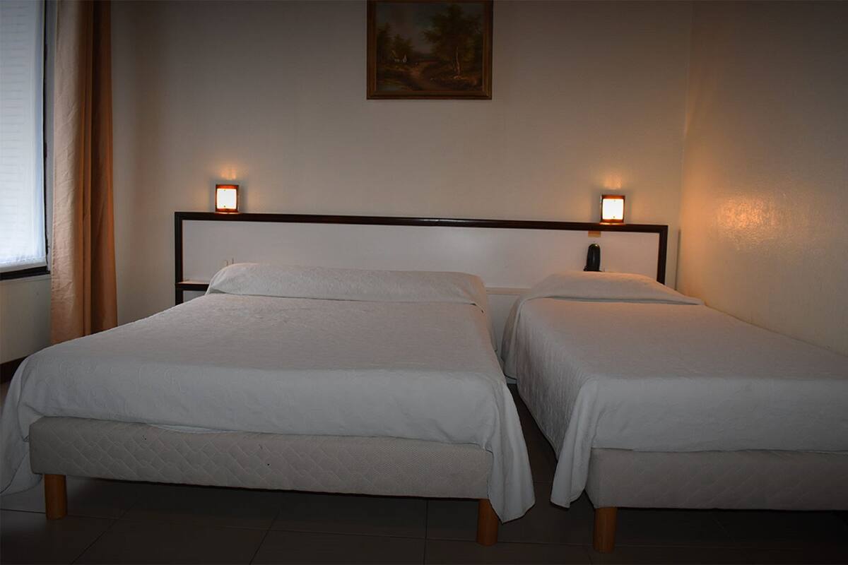A hotel room with two single beds, a painting on the wall, and two bedside lamps.