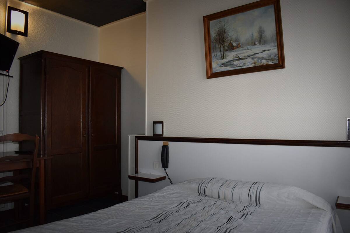 A bedroom with a bed, wooden wardrobe, bedside table, and a painting on the wall.