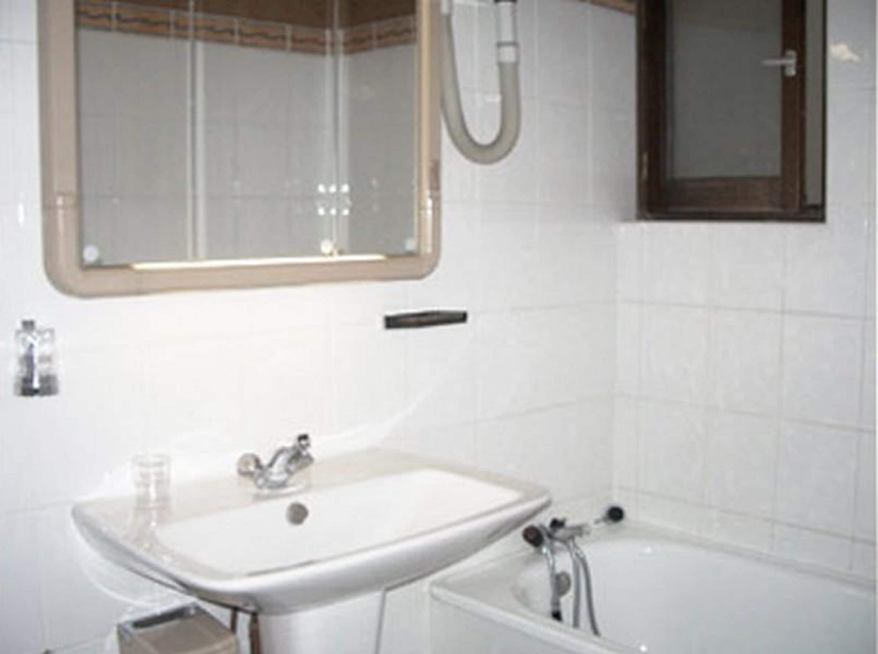 Une salle de bain avec un lavabo blanc, un miroir et une baignoire.