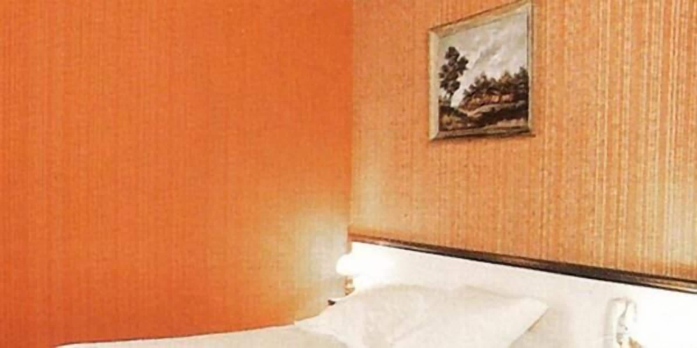 A hotel room with a bed, a painting on the wall, and a window.